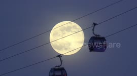 Cable cars pass in front of full snow moon as they cross London's River Thames
