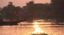 A small local car ferry traveling across a river at sunset in Thailand.
