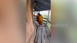 Buddhist monk terrified of heights walks along wooden bridge on edge of mountain