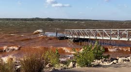 High winds causing wave to crash into floating dock and crashing into rocky shore.