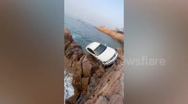 Man's rush to work nearly ends in disaster as car hangs off rocks near sea in China