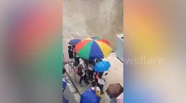 Crowd flocks under passerby’s huge umbrella as rain starts pouring