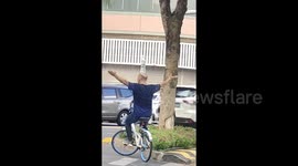 Chinese man balances bottled water on head while cycling on streets