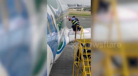 Airport workers remove tape strapped on plane's wing as worried passengers board
