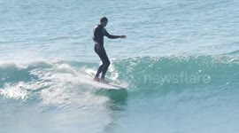 UK Weather. Sunshine and balmy weather lures crowds to a seaside resort, Surfers on longboards glide to the beach. Fistral beach, Newquay, Cornwall