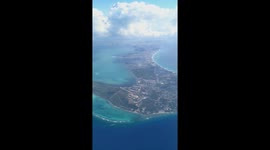 Flying Over Grand Cayman of the Cayman Islands from the sky filmed from Boeing 777 airplane through cabin window with depiction of engine