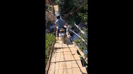 A man riding a motorbike crosses a suspension bridge damaged by flash floods