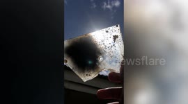 Curious resident watches rare hybrid solar eclipse behind broken glass