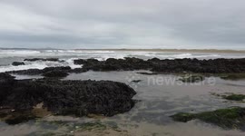 2.7K Low flyover beach rocks, shoreline and waves going out to sea at Rhosneigr, wales.