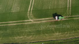 Drone footage of a Green Farm Tractor driving in field and spreading fertiliser on growing crop