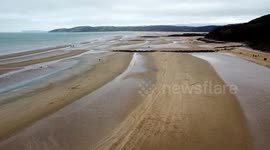 A drone shot of long sand bar beach with sea and people walking with dogs