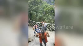 Mum and son sit on portable chair to be carried by workers to the top of mountain in China