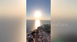 Spectacular sunset appears before relaxing tourists at cliffside beach in Greece