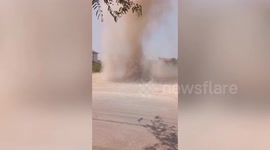 Gigantic dust devil tears through dirt field next to road