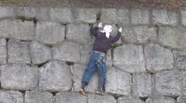 Man cleans castle walls above moat without a harness
