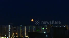 Plane flies in front of eerie bright orange 'Strawberry Full Moon' over St. Petersburg, Russia