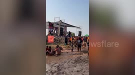 Festival-goers wallow and dance in mud in front of live band