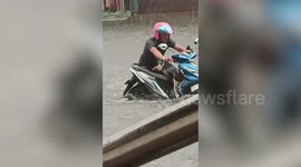 Loving pet owner puts dog safely on motorcycle while walking across flooded street