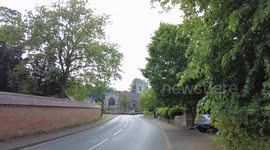 Walking past church bells ringing a green bus is parked outside old traditional English village