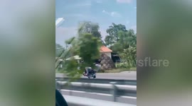 Driver talks on phone while doing wheelie on his scooter along highway in Cambodia