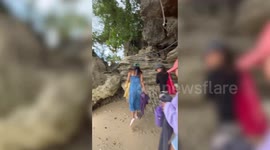 Distracted tourist bangs head on hanging sharp rock formations while walking on beach