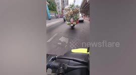 Overloaded motorcycle with tall stack of fresh vegetables cruises along busy road in Thailand