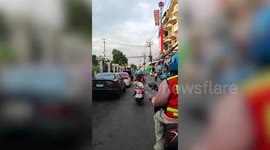 Pet cat sits behind scooter rider while travelling along market