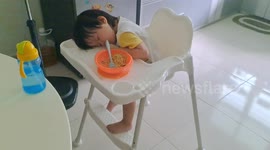 Two-year-old toddler falls asleep on baby chair while eating noodle by her dad