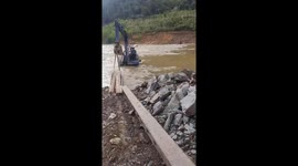 The excavator driver controls an excavator moving concrete power poles through flood water to repair electricity in the village