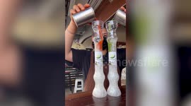 Barista pours ice-cold juice topped with whipped cream in quirky science lab glasses
