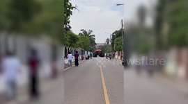 Two pick-up trucks with ridiculously-big wheels travel along road in Thailand