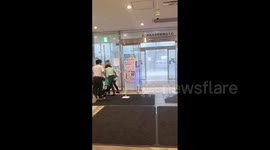 Supermarket staff attempt to close automatic doors as intense rain and wind batters Tokyo