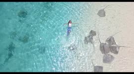 Beachgoer floats on her back above string rays in the Maldives