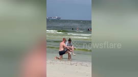 Chivalrous boyfriend forms a bench with his legs so woman can tie her shoes on beach