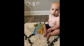 Cute little baby wants his mother to read him his favourite book by pointing at the pages