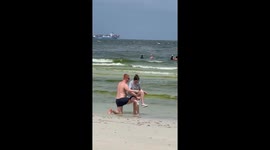 Chivalrous boyfriend forms a bench with his legs so partner can tie her shoes on beach