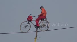 Martial artist rides bike on slack line high in the air