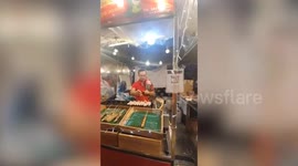 Street food vendor cooks grilled crocodile meat while holding sleeping baby croc