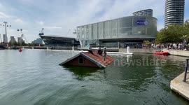 People fight for survival on the roof of a flooded house in the Royal Victoria Docks in London during the performance 'Sliding Slope'