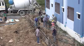 Thai construction workers use teamwork to move mixed concrete from a mixer truck, and move it to where it's required using plastic buckets.