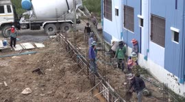 Team work Thai style on a small construction site, where workers from a line and manually transport mixed concrete by hand using plastic buckets.
