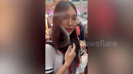 Pet snake slithers around schoolgirl's shoulders at exotic animal fair in Bangkok