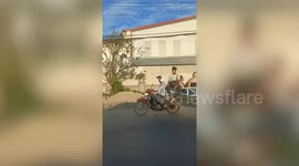 Tourist sit behind modified motorcycle with long cart in Cambodia