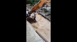 Residents sit in backhoe bucket to cross raging river amid floods in the Philippines