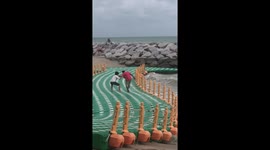 Two men hilariously struggle with floating sea dock being battered by waves