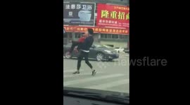 Young man picks up elderly lady to help her cross busy road