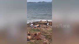 Wind blows man's shirt over his head as he struggles along coast