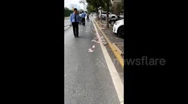 Bystanders guard hundreds of scattered Chinese notes on road until police arrive