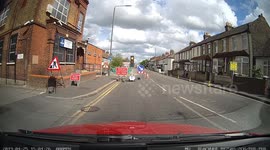 Impatient driver overtakes a line of traffic at temporary lights narrowly missing a car