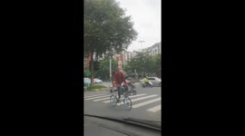 Gymnastic cyclist crosses road with water bottle balanced on head and one leg in the air